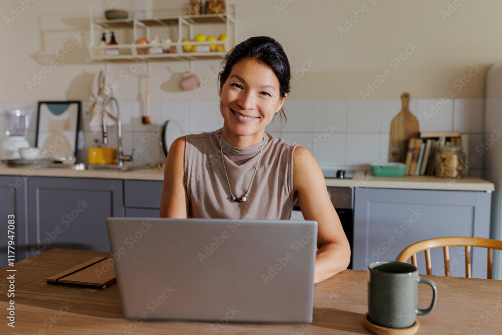 Woman working from home using laptop in kitchen Woman working from home using laptop in kitchen