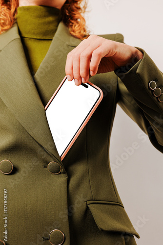 Woman putting smartphone with blank screen in green blazer photo