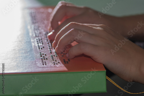 Hands of a little blind child reading the title of a book in Braille photo