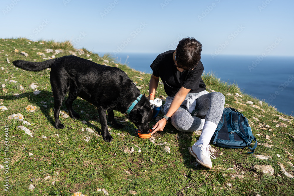 Hiker woman feeding her black labrador dog during hiking trip Hiker woman feeding her black labrador dog during hiking trip