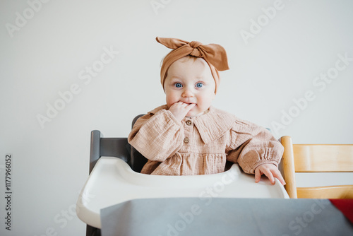 baby girl with big blue eyes sits in highchair looking around. photo