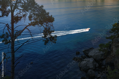 Boater navigating calm blue waters near rocky shoreline  photo