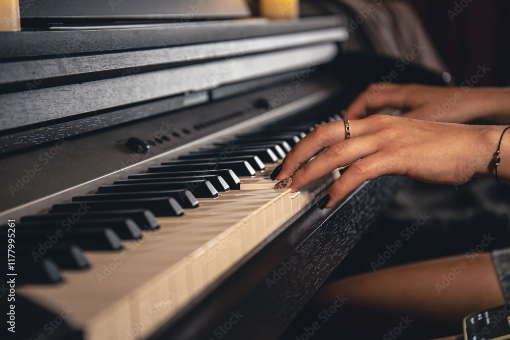 Fototapeta premium Female hands playing the piano. There are candles on the piano. Side view with background.