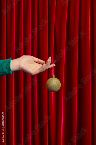 Hand Holding Christmas Ornament Against Red Curtain Background photo