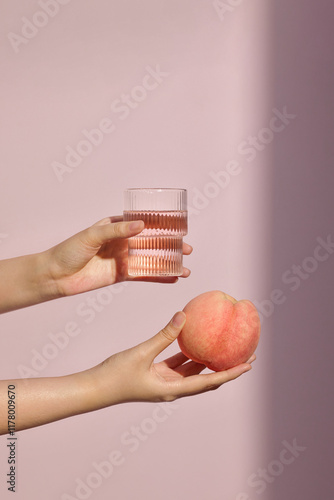 A delicate hand holds a ripe peach against a soft pink background photo