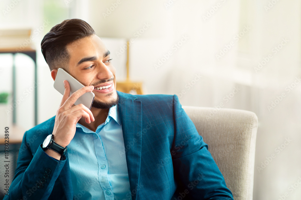Joyful Arab entrepreneur in business suit talking on cellphone at office, sitting in armchair, having conversation with friend or customer. Office worker in formal wear speaking on smartphone indoors Joyful Arab entrepreneur in business suit talking on cellphone at office, sitting in armchair, having conversation with friend or customer. Office worker in formal wear speaking on smartphone indoors
