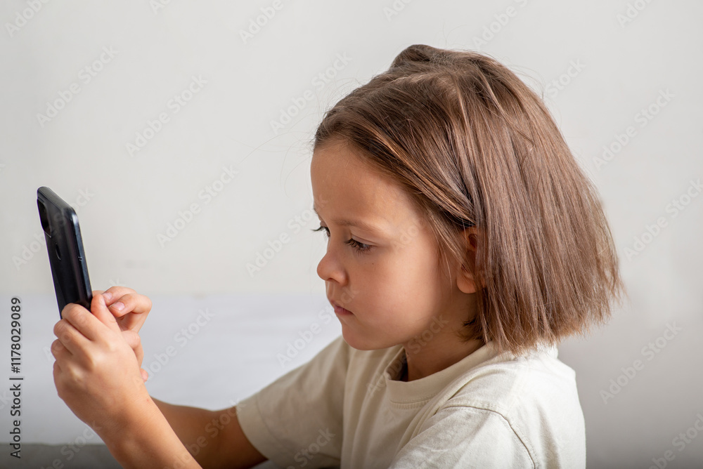 Little child uses the phone on a light background with copyspace Little child uses the phone on a light background with copyspace