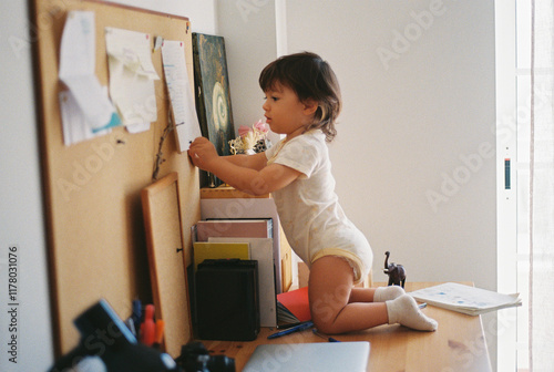 Toddler exploring papers on a home corkboard photo