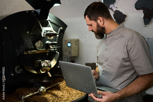 Barista roasting coffee beans in a workshop while using a laptop photo