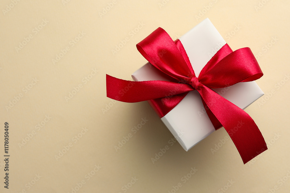 Beautiful gift box with red bow on beige background, top view. Space for text