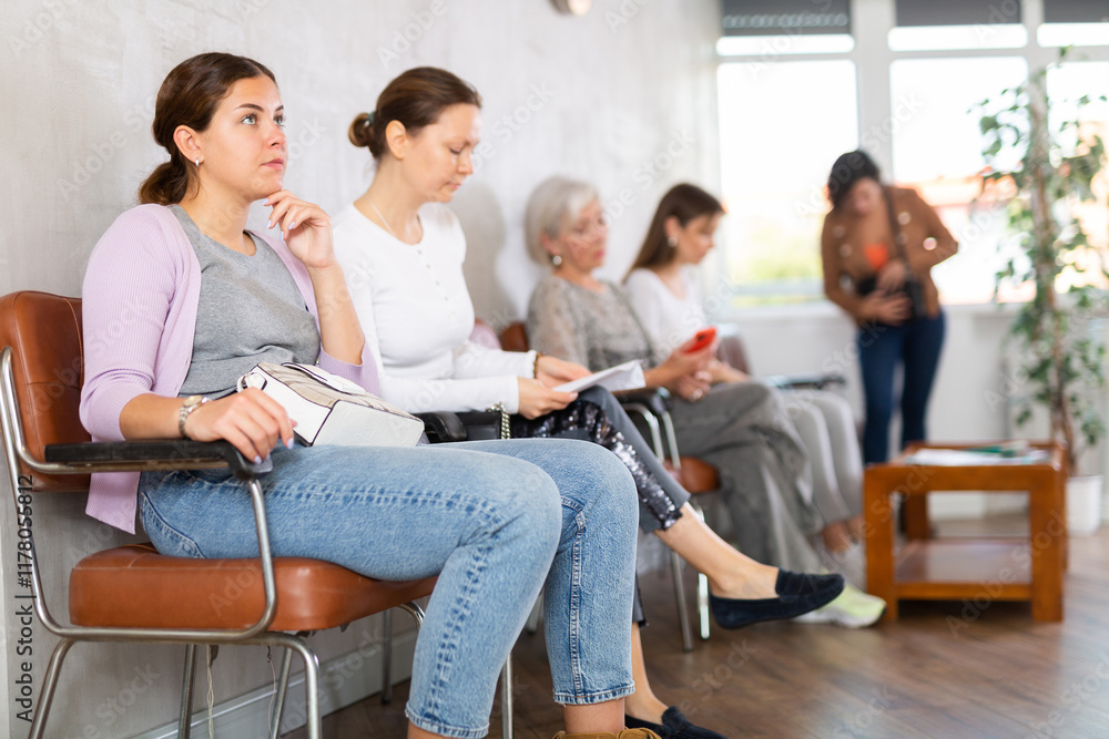 Young focused woman in casual clothes waiting for her turn while sitting on chair in reception.. Young focused woman in casual clothes waiting for her turn while sitting on chair in reception..