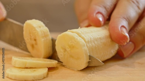 Female hands cutting and slicing yellow banana with knife on wooden board