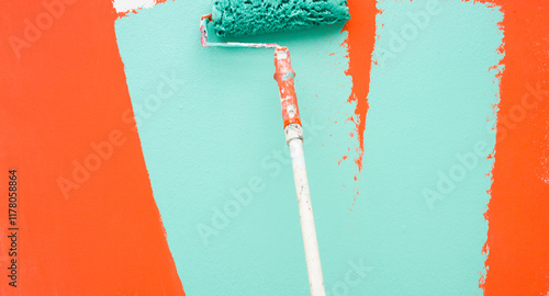 A paint roller is painting with green and orange colors indoors photo