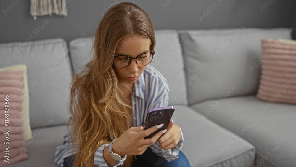 Young woman with blonde hair and glasses using smartphone in a cozy living room with grey couch Young woman with blonde hair and glasses using smartphone in a cozy living room with grey couch