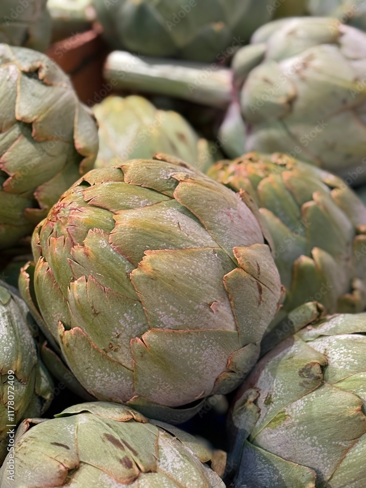 Obraz premium Close-up of fresh artichokes displayed in a vibrant farmers market setting. The image captures the natural texture and earthy color of the vegetables, emphasizing organic freshness and healthy eating.
