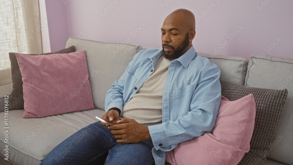 Young man with beard using phone in living room, sitting on couch inside apartment, relaxed, home interior, casual attire Young man with beard using phone in living room, sitting on couch inside apartment, relaxed, home interior, casual attire