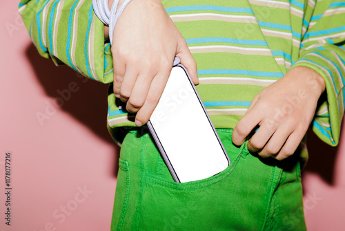 Woman putting smartphone with blank screen in green jeans pocket