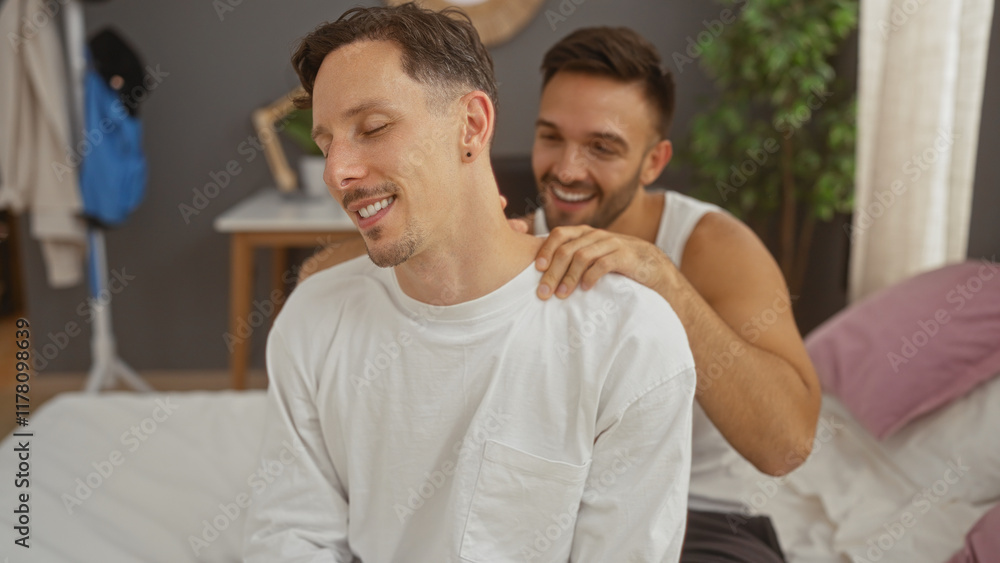 Fototapeta premium Men in a bedroom with one giving the other a back massage while sitting on a bed and smiling
