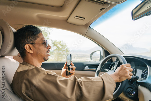 Arab man driving car while using smartphone: photo