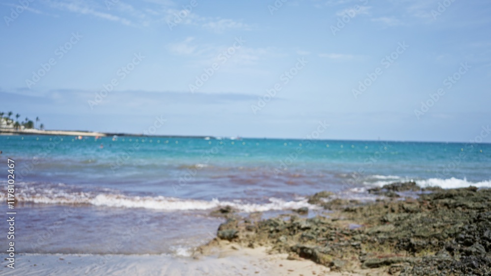 Blurred beach scene with defocused view of ocean, waves, and rocky shoreline under a clear sky. Blurred beach scene with defocused view of ocean, waves, and rocky shoreline under a clear sky.