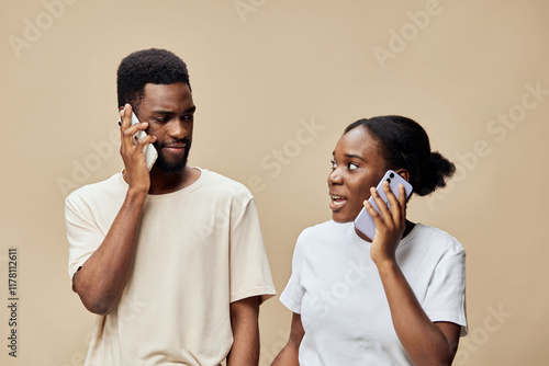 Young African American couple talking on the phone, dressed in casual clothing against a neutral brown background, showcasing connection and communication photo