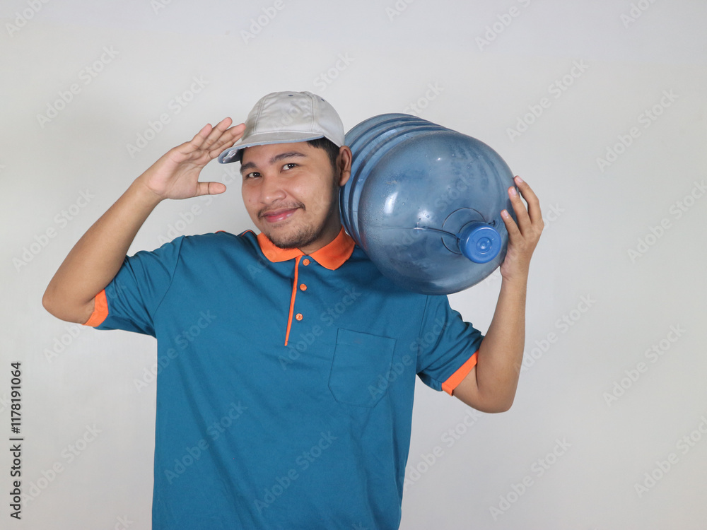 A happy Asian delivery courier is carrying a gallon or big water bottle of mineral water with a gesture of respect as a sign of being ready to deliver the gallon at any time A happy Asian delivery courier is carrying a gallon or big water bottle of mineral water with a gesture of respect as a sign of being ready to deliver the gallon at any time
