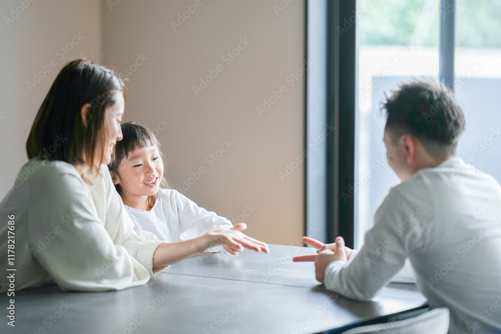 A Japanese parent and child, a woman in her 30s, a man in his 20s, and a 6-year-old girl, are playing with their hands at a table in their living room. A Japanese parent and child, a woman in her 30s, a man in his 20s, and a 6-year-old girl, are playing with their hands at a table in their living room.