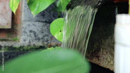 Small artificial waterfall surrounded by lush green plants, creating a peaceful and serene natural setting. Ideal for garden design, tranquility themes, and outdoor aesthetics.