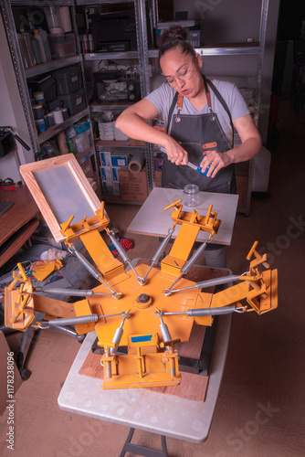 Young white-skinned Latina woman doing printing work using the screen printing and printing with meshes method. It could be for industry or sales. Advertising uses different tools or objects. She is h photo