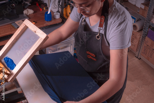 Young white-skinned Latina woman doing printing work using the screen printing and printing with meshes method. It could be for industry or sales. Advertising uses different tools or objects. She is h photo