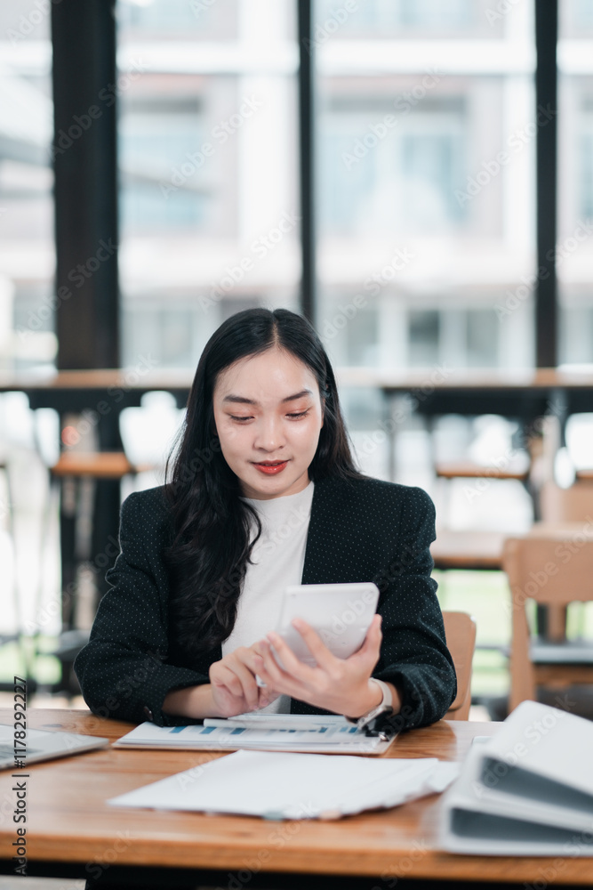Businesswoman in a modern office using a smartphone, surrounded by documents and a laptop, with large windows in the background. Businesswoman in a modern office using a smartphone, surrounded by documents and a laptop, with large windows in the background.