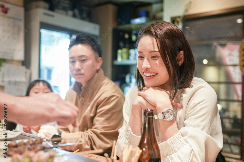 A Japanese parent and child, a woman in her 30s, a 6-year-old girl, and a man in his 20s, are enjoying yakitori at an izakaya. A Japanese parent and child, a woman in her 30s, a 6-year-old girl, and a man in his 20s, are enjoying yakitori at an izakaya.