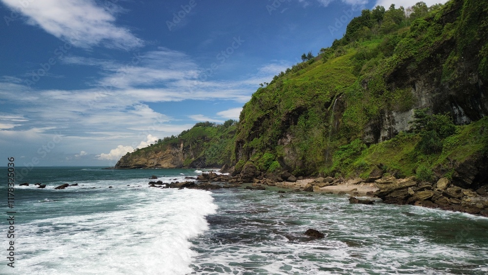 Aerial drone view of coastline with hills and trees, as well as view of coral cliffs and sea with waves from the ocean in Menganti Beach Kebumen Central Java Indonesia Aerial drone view of coastline with hills and trees, as well as view of coral cliffs and sea with waves from the ocean in Menganti Beach Kebumen Central Java Indonesia