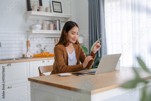 Fotografie Beautiful young Asian woman working with laptop computer in home kitchen