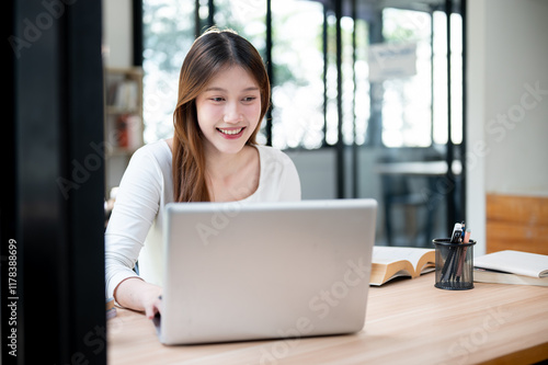 A smiling, happy Asian female college student working on her project on her laptop in a coffee shop. Free Download A smiling, happy Asian female college student working on her project on her laptop in a coffee shop. - GFXLoad