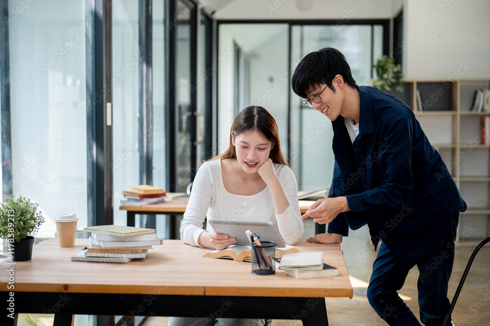 Two positive Asian college students are looking at a tablet screen and discussing. Two positive Asian college students are looking at a tablet screen and discussing.
