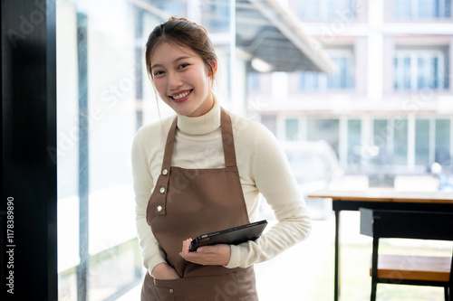 A smiling, friendly Asian female coffee shop waitress or barista is standing in her coffee shop. Free Download A smiling, friendly Asian female coffee shop waitress or barista is standing in her coffee shop. - GFXLoad