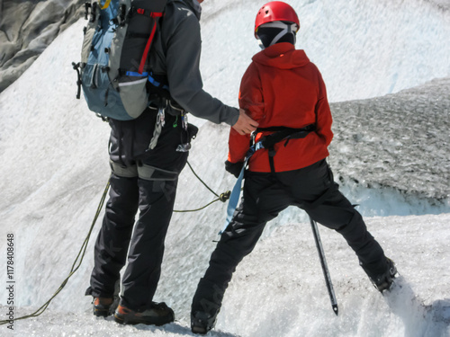 GenZ male viewed from behind being helped as he is exploring the running water in a cracked glacier while hiking Mendenhall Glacier in Juneau. Alaska and wearing the appropriate gear for it. photo