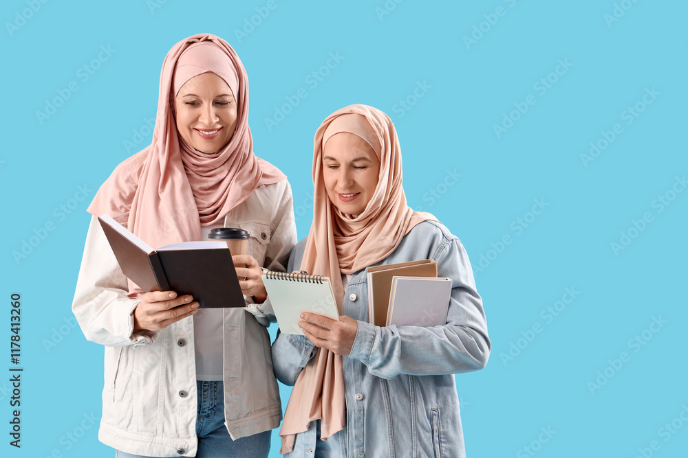 Mature Muslim women in hijabs with books and coffee on blue background Mature Muslim women in hijabs with books and coffee on blue background
