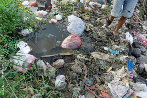 A man walks past piles of household waste and factory waste that pollute the river water.
