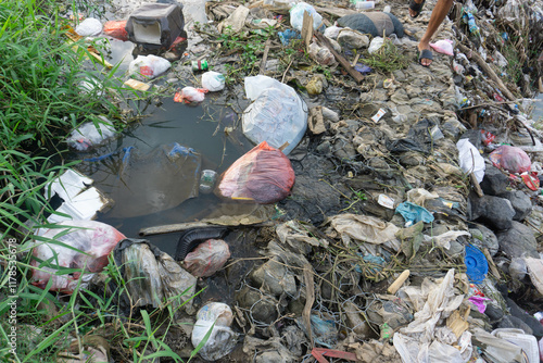 A man walks past piles of household waste and factory waste that pollute the river.