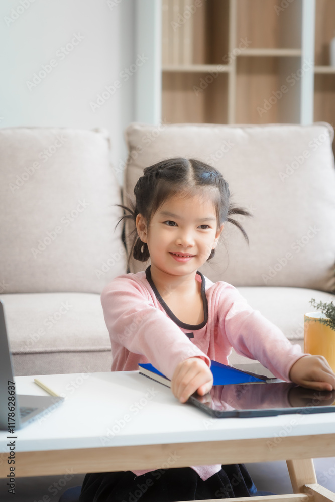 An Asian female and her daughter sit on the sofa in the living room during the day, using a laptop, headphones, and mobile device while studying at the desk with books around them. An Asian female and her daughter sit on the sofa in the living room during the day, using a laptop, headphones, and mobile device while studying at the desk with books around them.