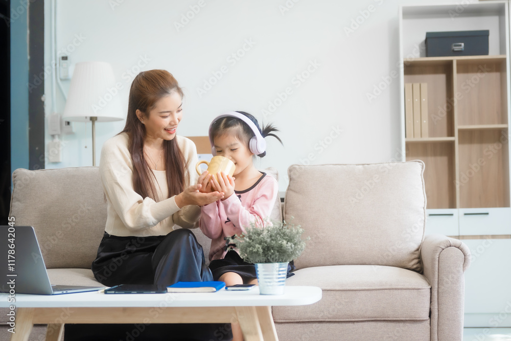 Asian young mother and her daughter sit together on the sofa in the cozy living room, working on homework at the desk, creating a warm and supportive atmosphere for learning, love, hug, mother days. Asian young mother and her daughter sit together on the sofa in the cozy living room, working on homework at the desk, creating a warm and supportive atmosphere for learning, love, hug, mother days.