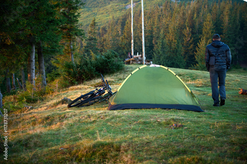 Man with bike near the tent in the mountains. Camping on the hill.  European biker resting after cycling mountain bike camping for the rest with tents and bicycles. Tourist life photo