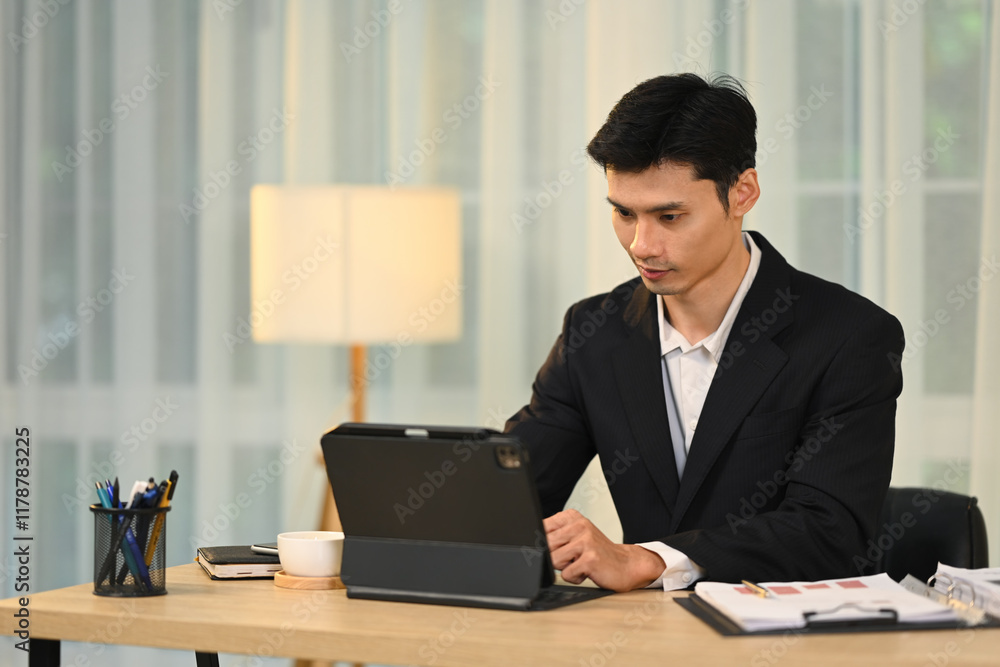 Focused millennial businessman in black suit working on digital tablet in modern office Focused millennial businessman in black suit working on digital tablet in modern office