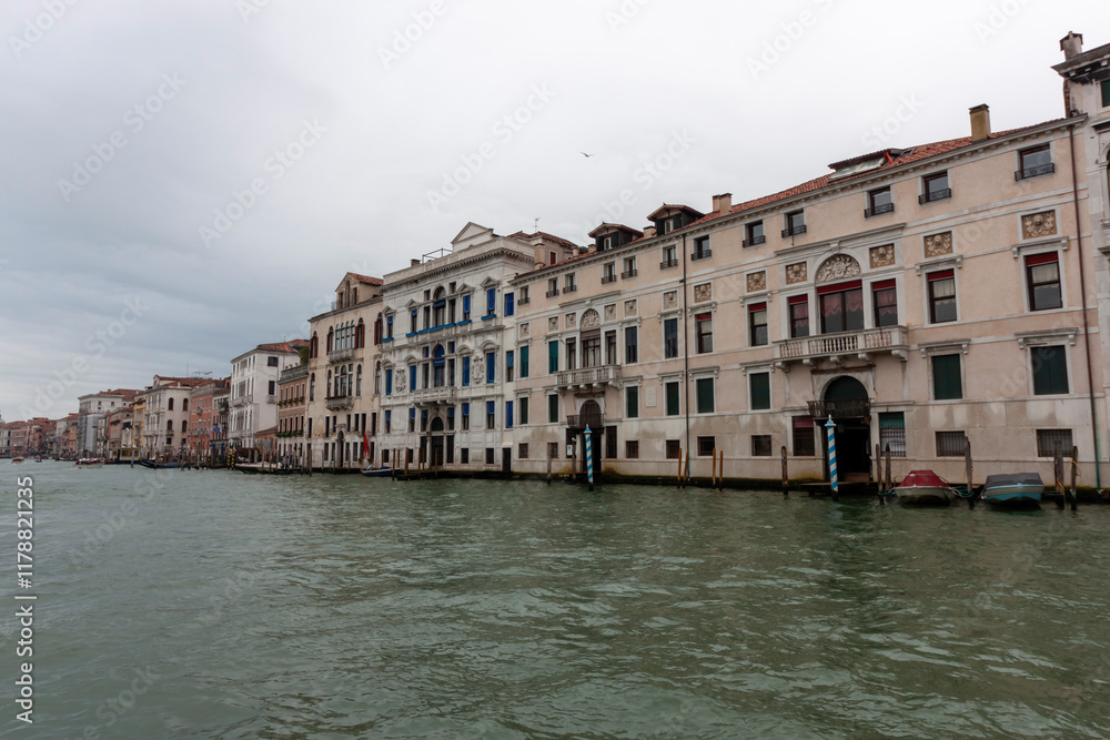 Fototapeta premium A panoramic view of the Grand Canal in Venice, Italy, showcasing the ornate facades of historic palazzi reflecting in the water. Several boats can be seen navigating the canal. Overcast sky