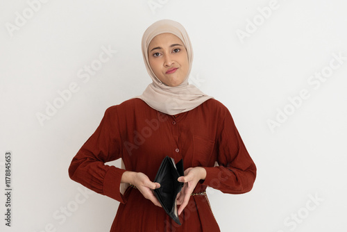 Sad young woman in a hijab looking up while holding an empty wallet, expressing financial difficulties or disappointment. photo