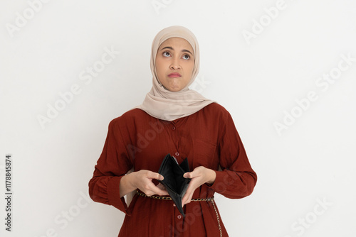 Sad young woman in a hijab looking up while holding an empty wallet, expressing financial difficulties or disappointment. photo