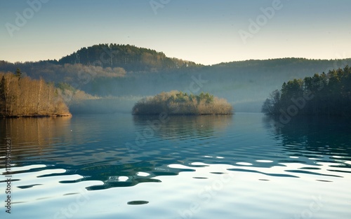 Masurian Lake District Serenity, Poland Calm lake reflecting hills and islands under a hazy sky. photo