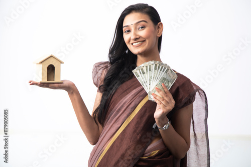 Blonde Housewife Holding Indian Currency And Toy House Against White Background